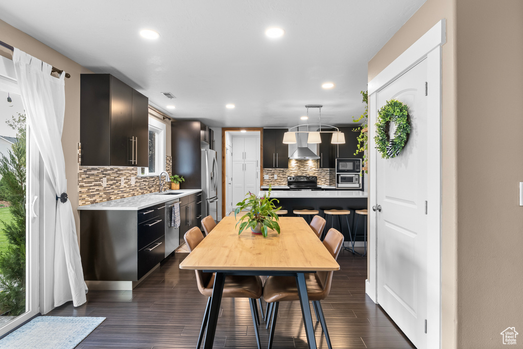 Kitchen featuring dark wood-type flooring, black appliances, decorative backsplash, and wall chimney exhaust hood