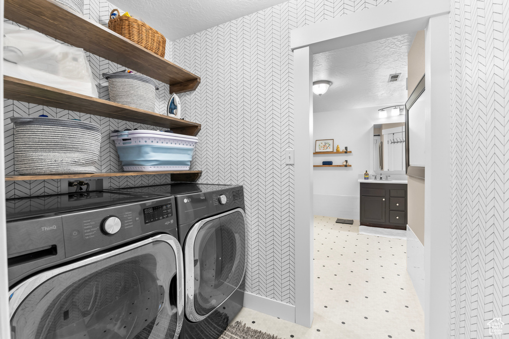 Clothes washing area featuring a textured ceiling, separate washer and dryer, and sink