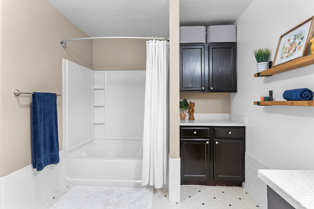 Bathroom featuring a textured ceiling, vanity, and shower / bath combination with curtain