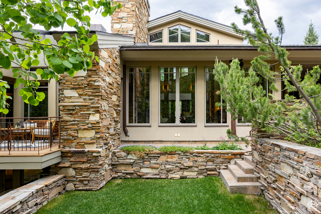 Property entrance with stucco siding, stone siding, a deck, and a yard