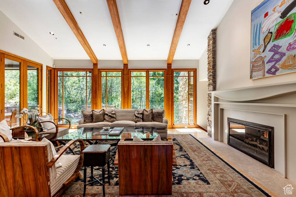 Living room with visible vents, vaulted ceiling with beams, and a glass covered fireplace