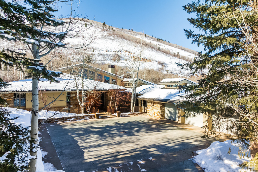 Snow covered rear of property featuring concrete driveway and stone siding