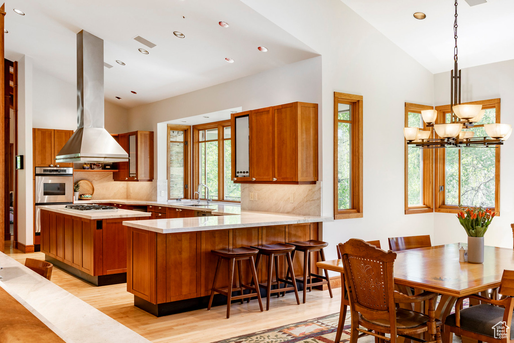 Kitchen with appliances with stainless steel finishes, light wood-style flooring, backsplash, brown cabinets, and range hood