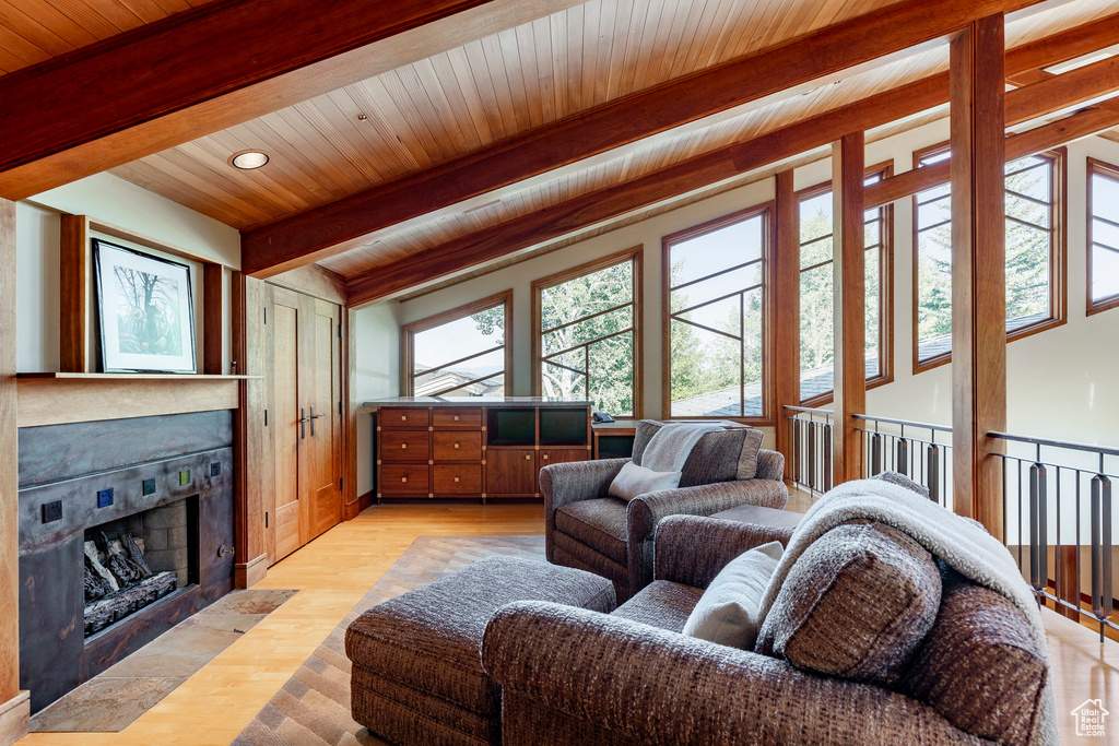 Living area featuring plenty of natural light, wooden ceiling with exposed beams, a tile fireplace, and light wood finished floors