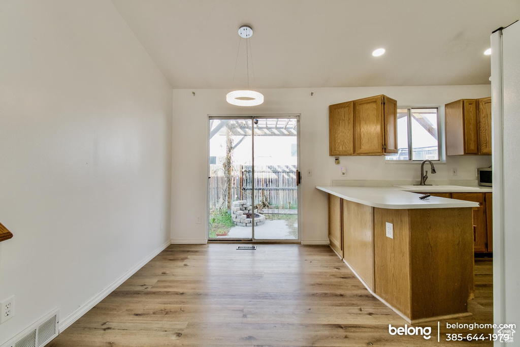 Kitchen featuring light wood-type flooring, hanging light fixtures, kitchen peninsula, and sink