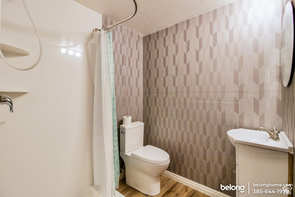 Bathroom with a shower with shower curtain, hardwood / wood-style floors, toilet, and vanity