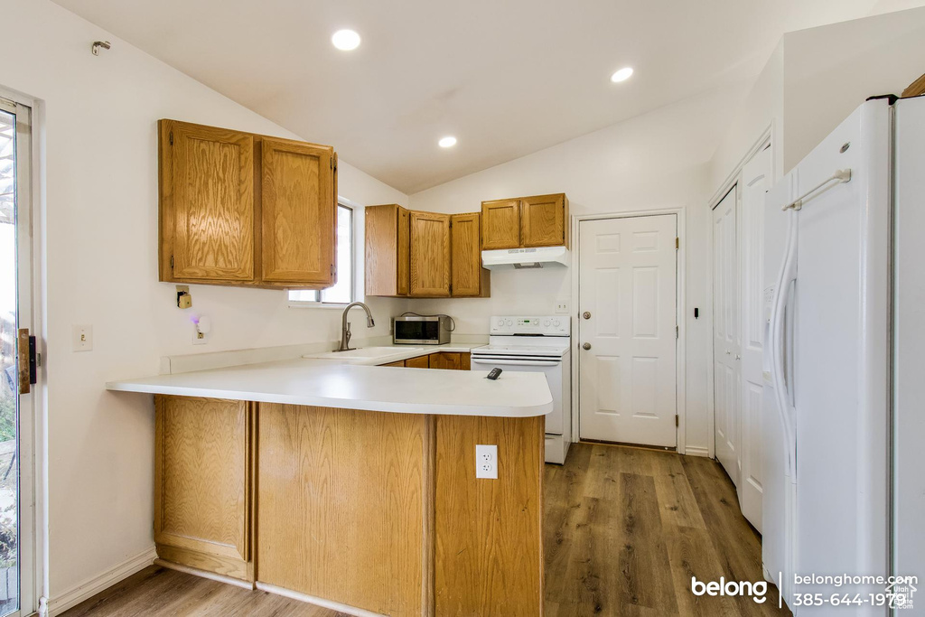 Kitchen with white appliances, wood-type flooring, kitchen peninsula, sink, and lofted ceiling