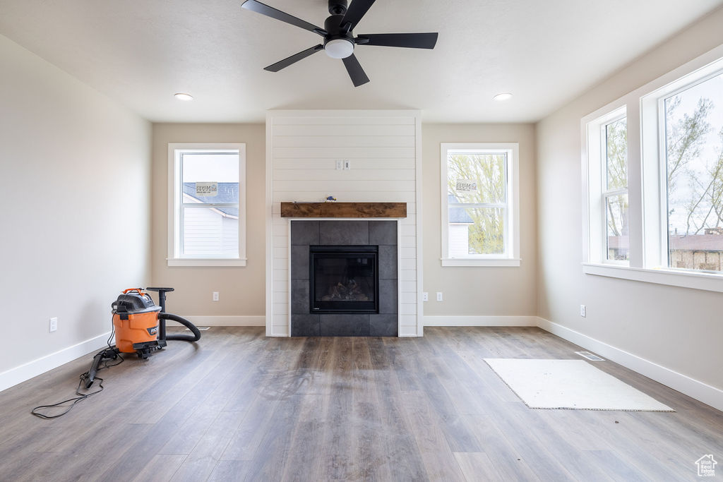 Unfurnished living room featuring a wealth of natural light, wood-type flooring, ceiling fan, and a tile fireplace