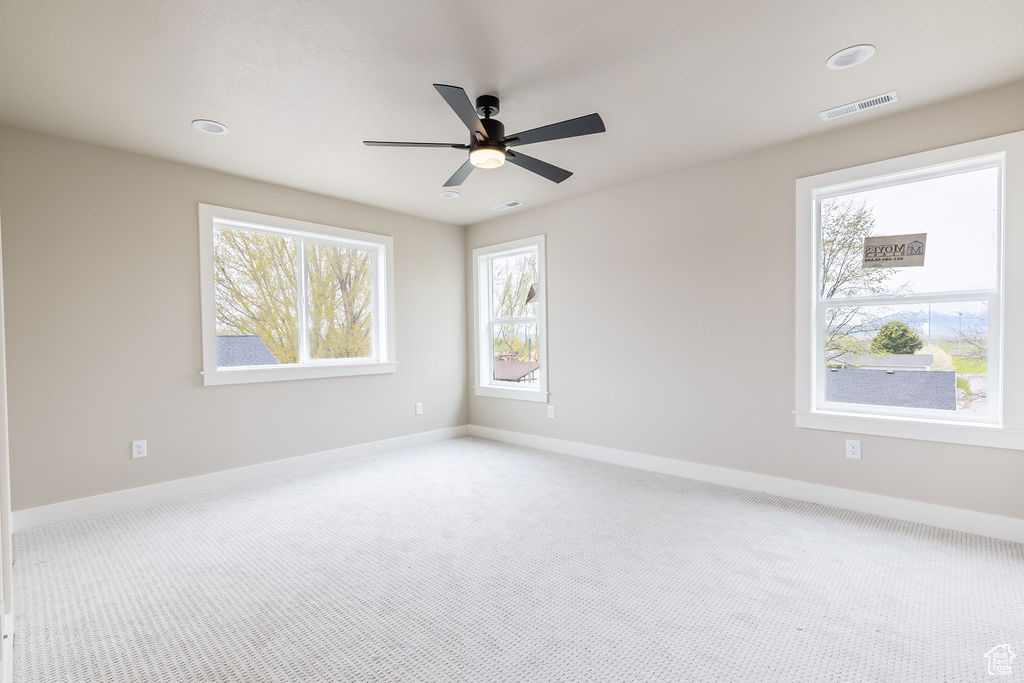 Empty room with a healthy amount of sunlight, ceiling fan, and carpet flooring