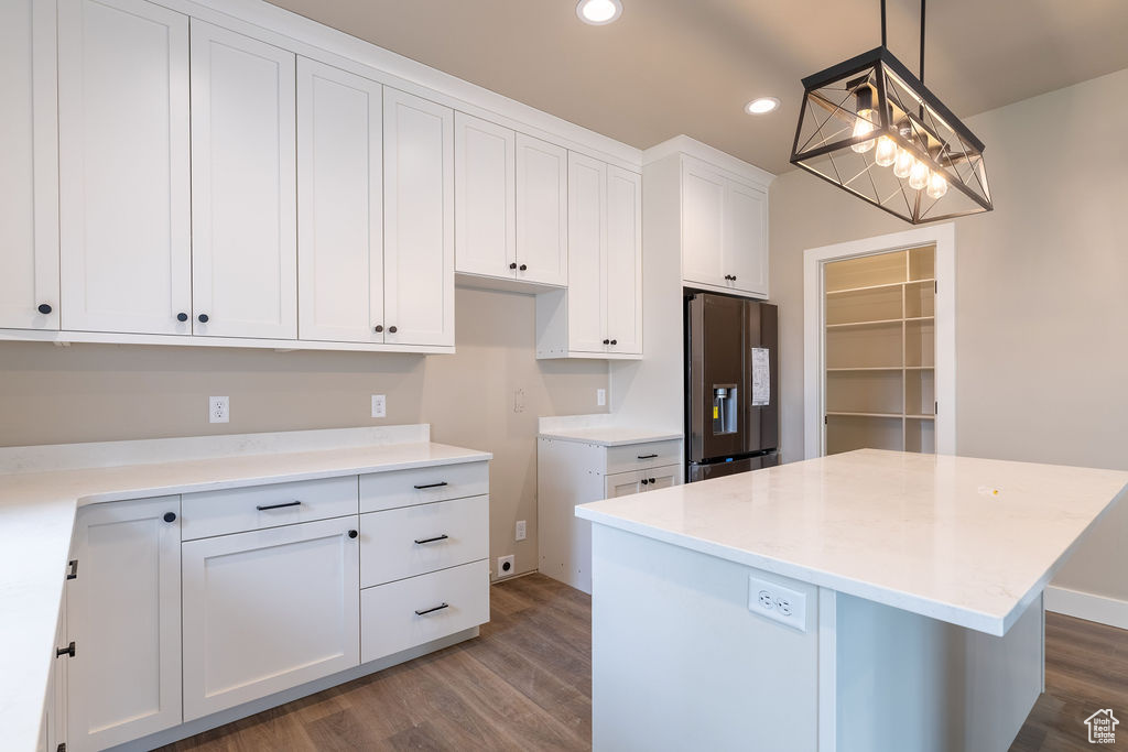 Kitchen featuring dark hardwood / wood-style floors, stainless steel fridge, decorative light fixtures, a center island, and white cabinetry