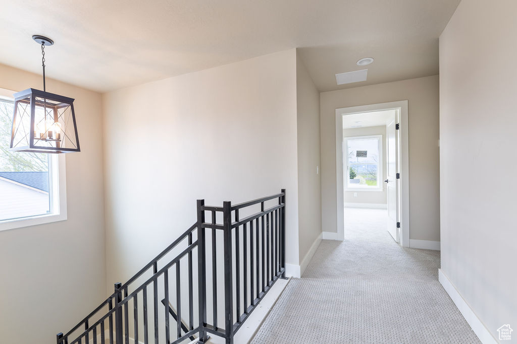 Hallway featuring an inviting chandelier and light carpet