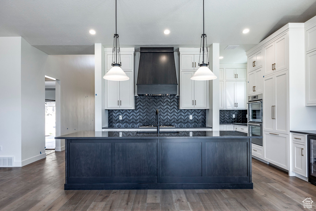 Kitchen featuring custom range hood, dark hardwood / wood-style floors, decorative light fixtures, and white cabinets