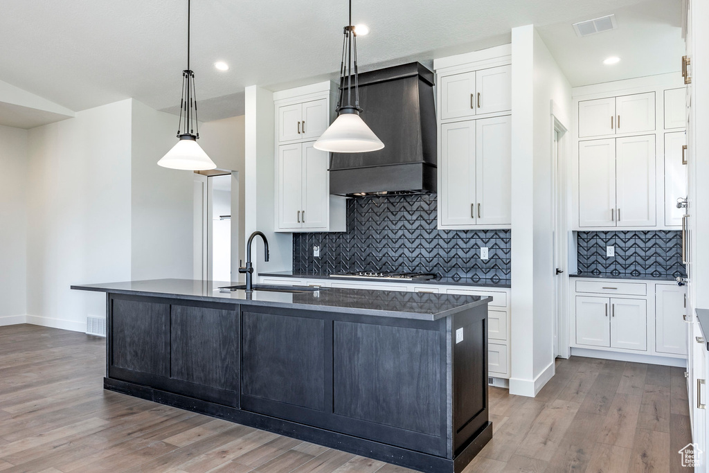 Kitchen featuring pendant lighting, sink, white cabinetry, custom exhaust hood, and light wood-type flooring