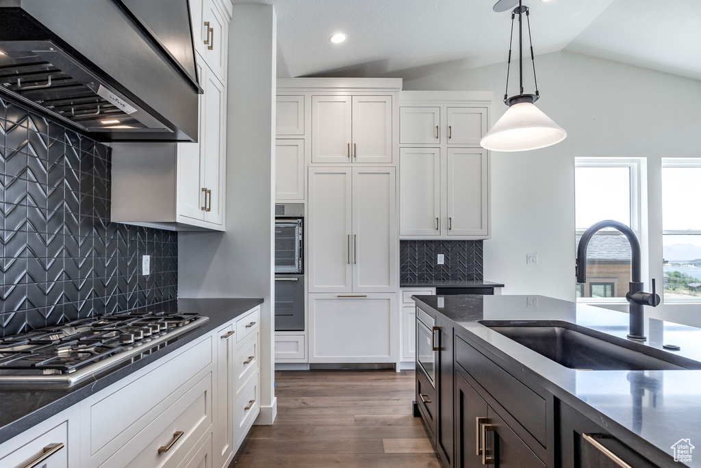 Kitchen with lofted ceiling, white cabinets, hanging light fixtures, and backsplash