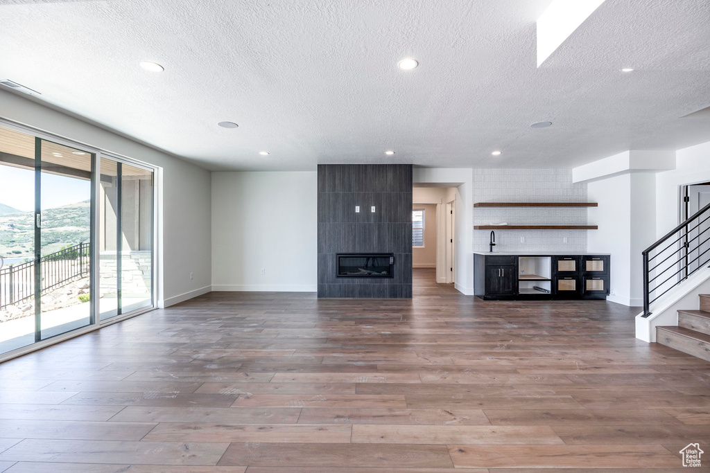 Unfurnished living room with a textured ceiling, hardwood / wood-style flooring, and a tile fireplace