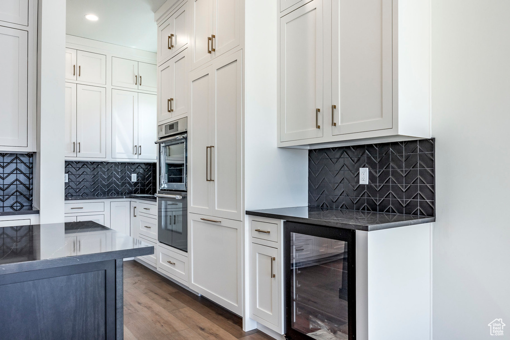 Kitchen featuring white cabinets, hardwood / wood-style floors, beverage cooler, double oven, and decorative backsplash