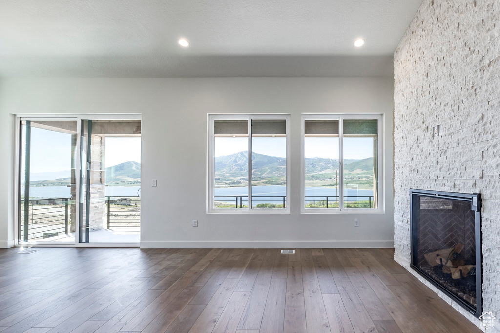 Unfurnished living room with dark wood-type flooring, a water and mountain view, and a fireplace