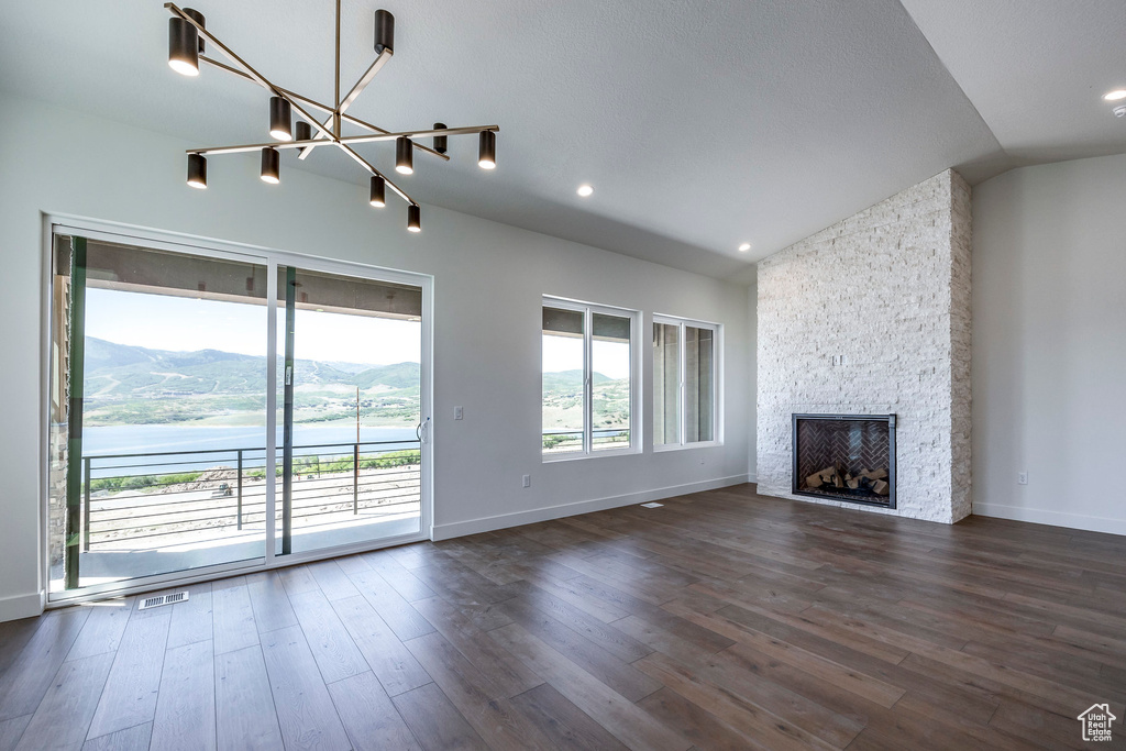 Unfurnished living room featuring a stone fireplace, dark wood-type flooring, a mountain view, and vaulted ceiling