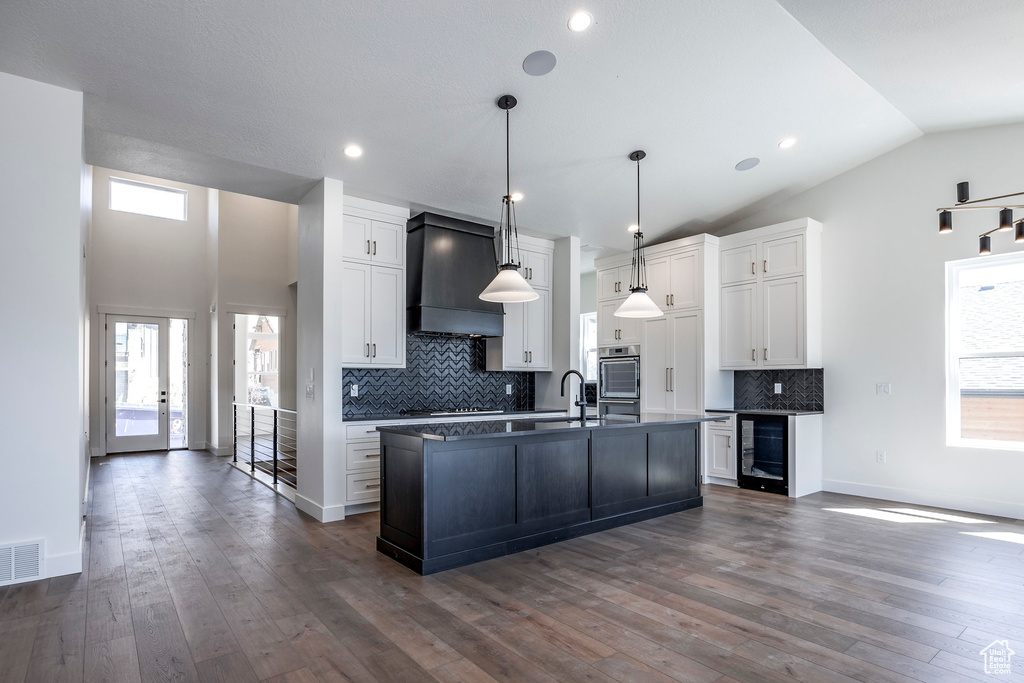 Kitchen with a kitchen island with sink, white cabinetry, dark hardwood / wood-style flooring, decorative backsplash, and custom range hood