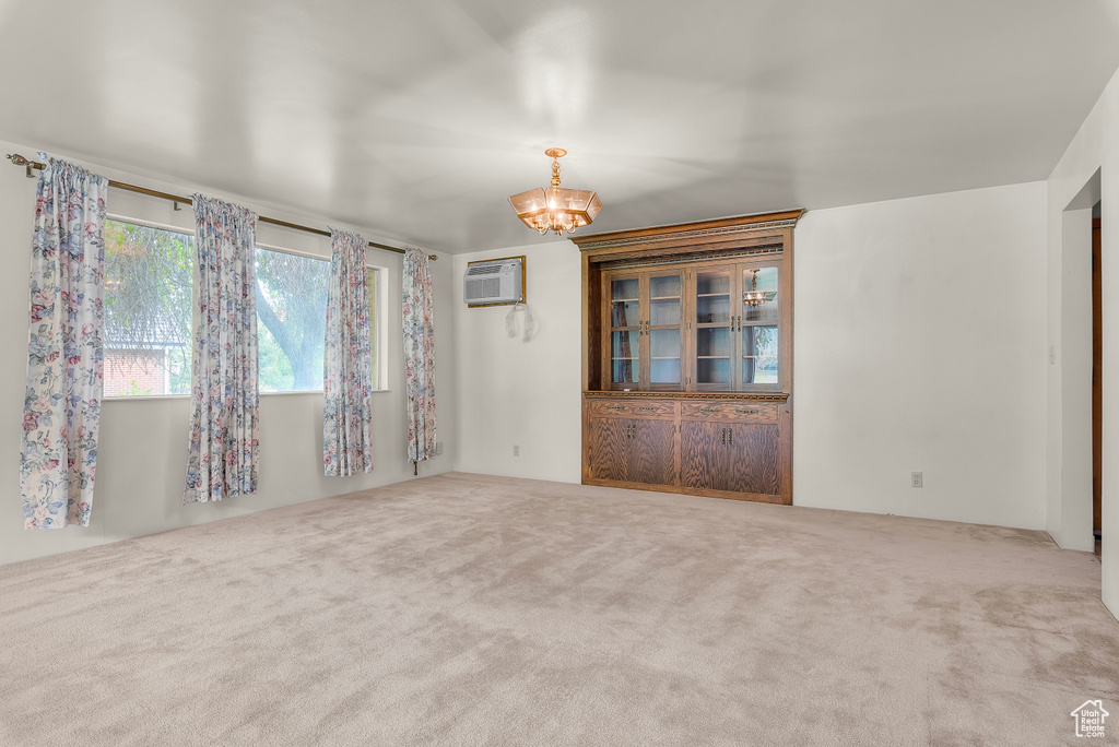 Spare room featuring carpet floors, a notable chandelier, and an AC wall unit