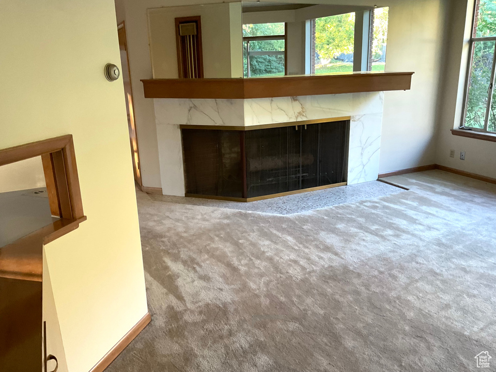 Unfurnished living room with carpet floors, a healthy amount of sunlight, and a high end fireplace