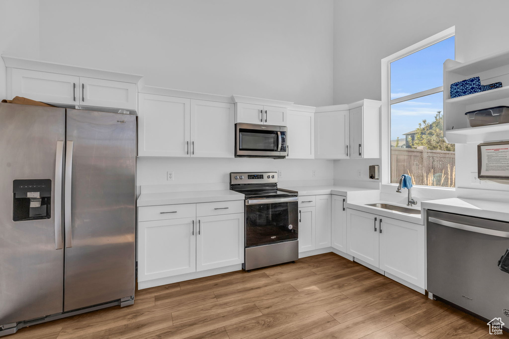 Kitchen with light wood-type flooring, stainless steel appliances, white cabinetry, sink, and a high ceiling