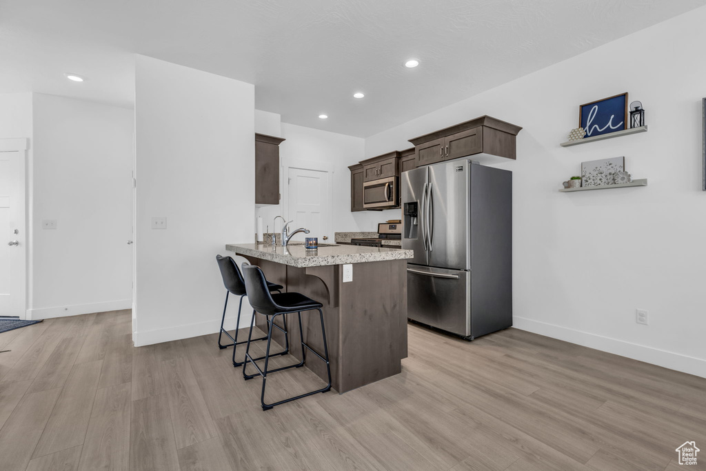 Kitchen featuring light wood-type flooring, stainless steel appliances, dark brown cabinets, kitchen peninsula, and a breakfast bar