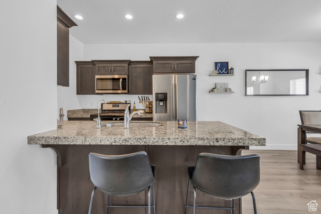 Kitchen featuring appliances with stainless steel finishes, light hardwood / wood-style floors, sink, kitchen peninsula, and a kitchen bar