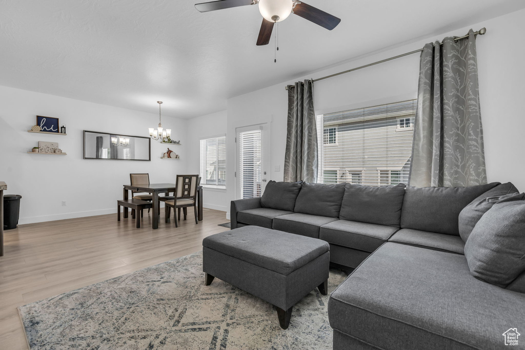 Living room featuring ceiling fan with notable chandelier and light hardwood / wood-style floors