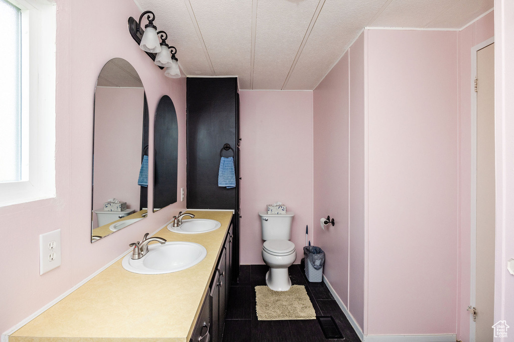 Bathroom with vanity, toilet, a textured ceiling, and a healthy amount of sunlight