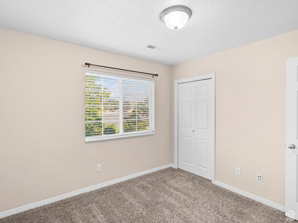 Unfurnished bedroom featuring a textured ceiling, carpet, and a closet