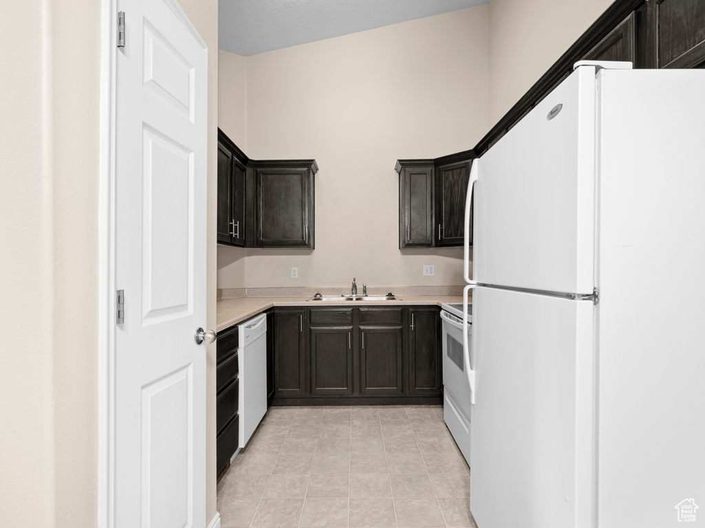 Kitchen with white appliances, sink, light tile patterned flooring, and dark brown cabinetry