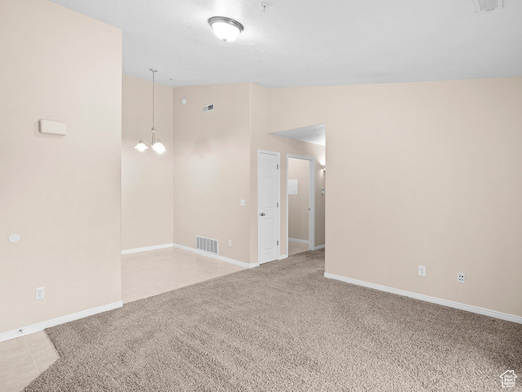 Spare room with light carpet, vaulted ceiling, and a notable chandelier