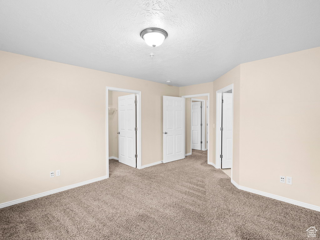 Unfurnished bedroom with a closet, a spacious closet, carpet, and a textured ceiling