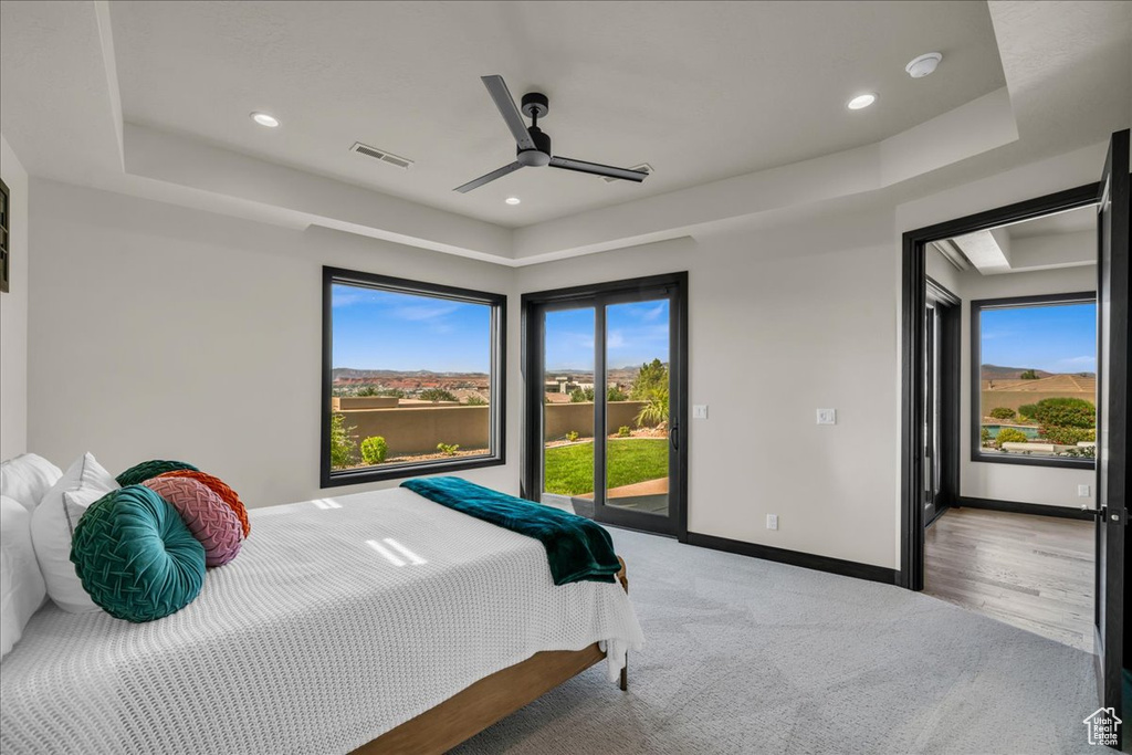 Bedroom featuring access to exterior, ceiling fan, a raised ceiling, and light hardwood / wood-style flooring