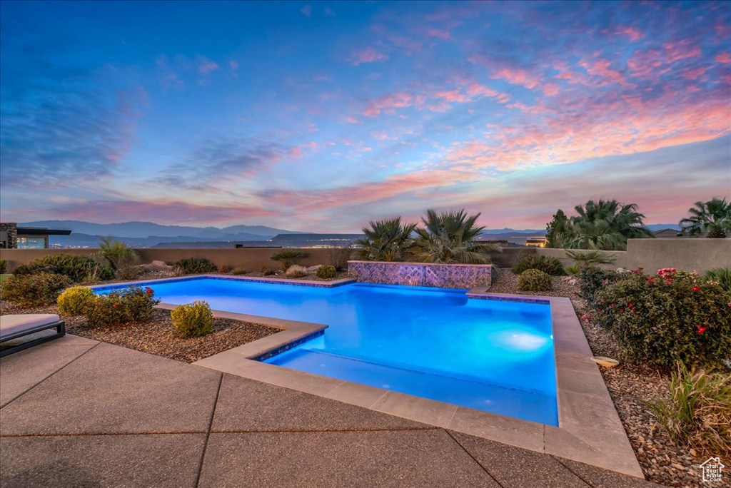 Pool at dusk featuring a mountain view and a patio area