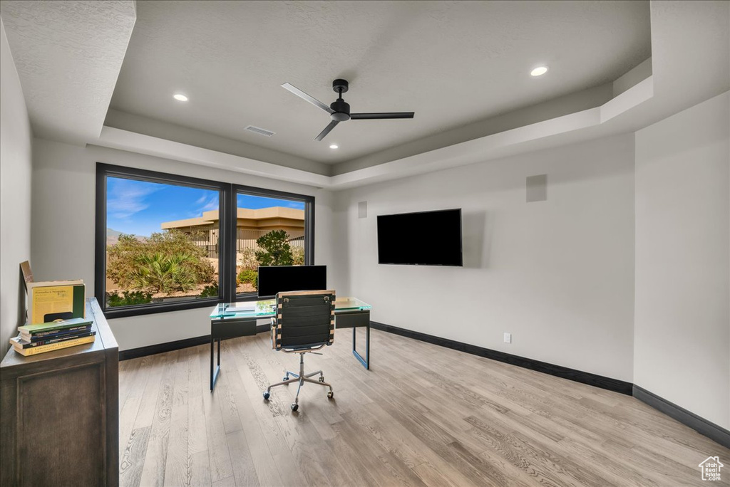 Home office with a tray ceiling, ceiling fan, and light hardwood / wood-style floors