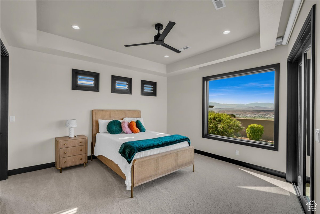 Bedroom with light carpet, a raised ceiling, and ceiling fan