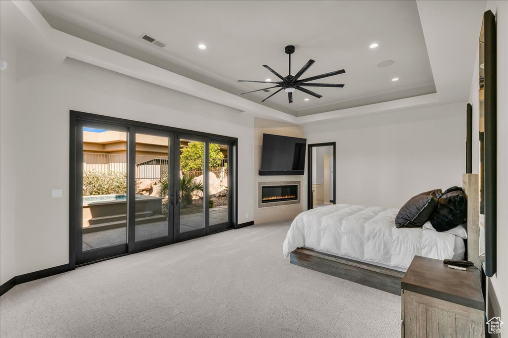 Carpeted bedroom with access to exterior, ceiling fan, and a raised ceiling