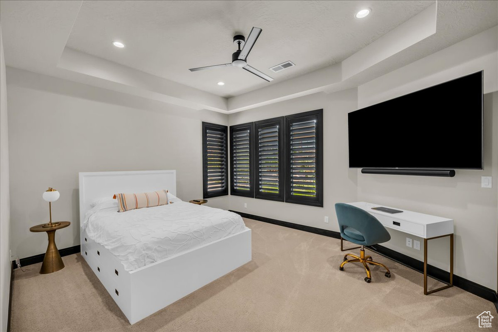 Bedroom featuring a raised ceiling, ceiling fan, and light carpet