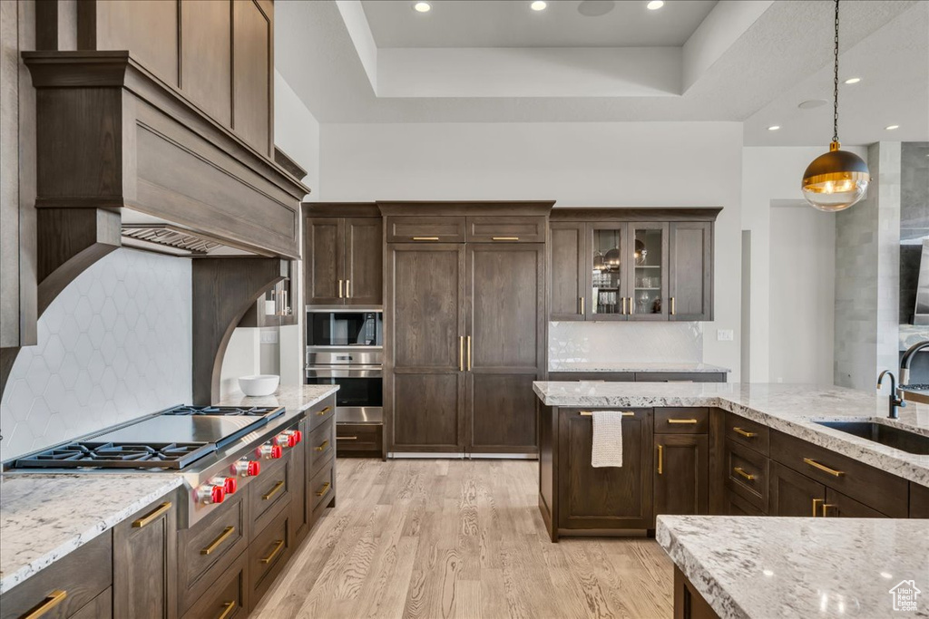 Kitchen with light stone counters, sink, decorative light fixtures, and light hardwood / wood-style floors