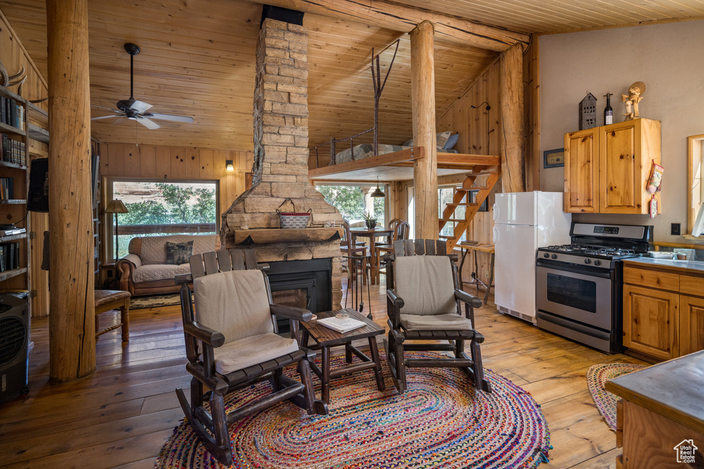 Living area featuring light wood finished floors, ceiling fan, wood ceiling, wooden walls, and high vaulted ceiling