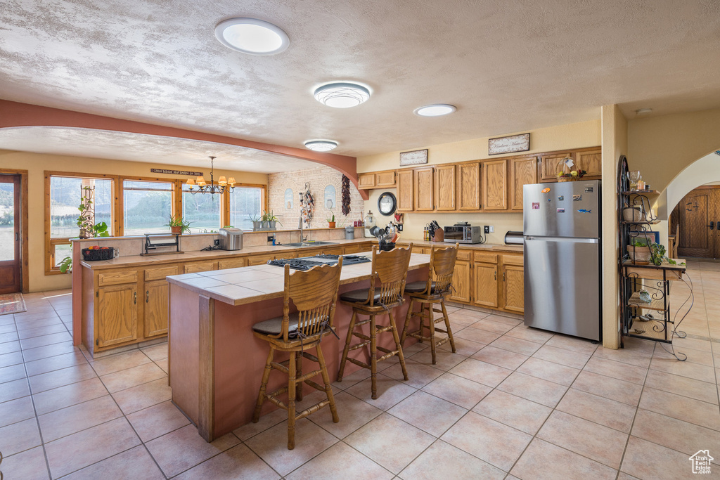 Kitchen with freestanding refrigerator, light tile patterned flooring, a peninsula, arched walkways, and tile counters