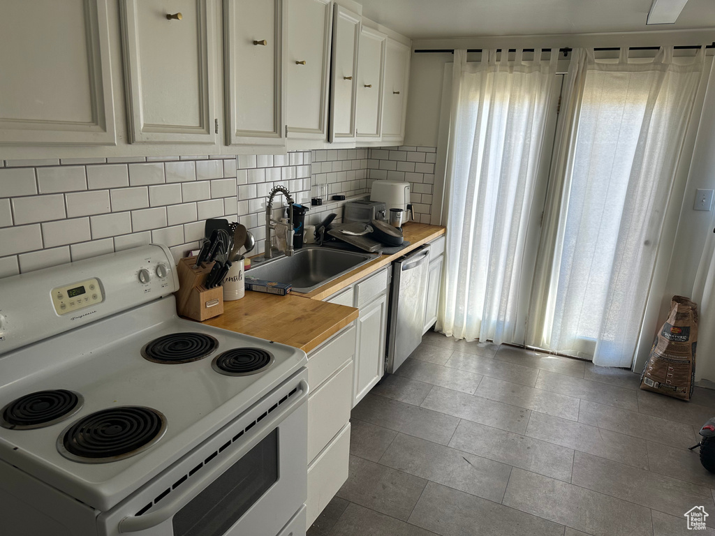 Kitchen featuring dishwasher, electric range, white cabinetry, sink, and decorative backsplash