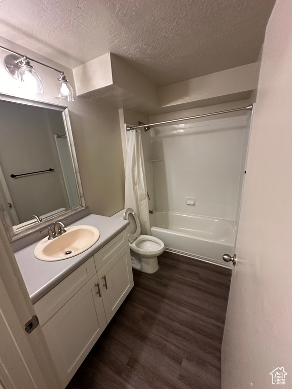 Full bathroom with hardwood / wood-style flooring, shower / tub combo, a textured ceiling, vanity, and toilet