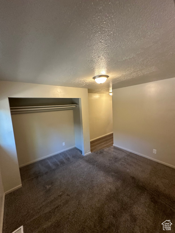 Unfurnished bedroom featuring a textured ceiling, a closet, and dark colored carpet