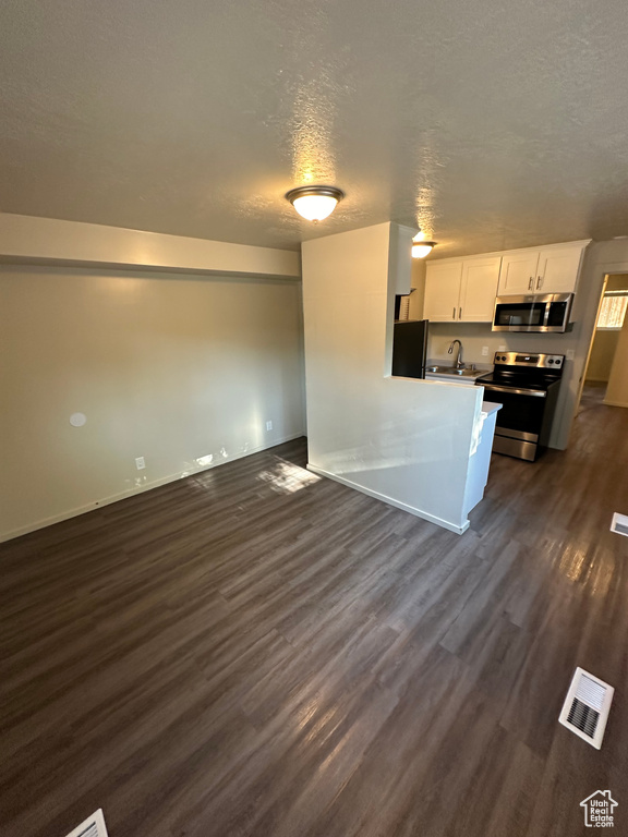 Kitchen with appliances with stainless steel finishes, white cabinetry, sink, a textured ceiling, and dark hardwood / wood-style flooring