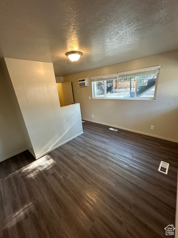 Spare room featuring a wall mounted AC, a textured ceiling, and dark hardwood / wood-style floors