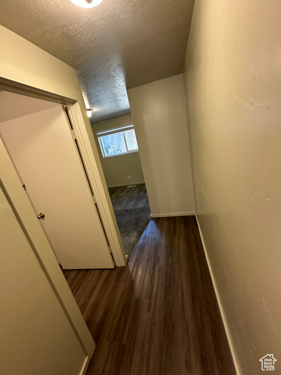 Hall with a textured ceiling and dark hardwood / wood-style floors