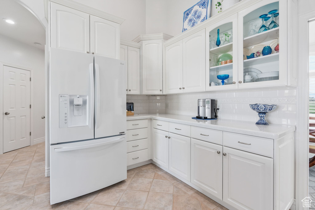 Kitchen with white refrigerator with ice dispenser, light tile patterned floors, decorative backsplash, and white cabinetry